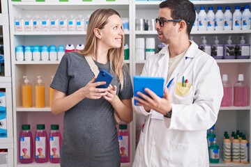 Man and woman pharmacist and pregnant client using smartphone and touchpad speaking at pharmacy
