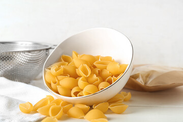 Bowl with raw conchiglie pasta on light wooden background