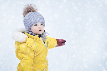 Happy toddler baby is playing in a yellow snowsuit. Child boy in warm clothes walks in snowy winter park. Kid aged one year six months