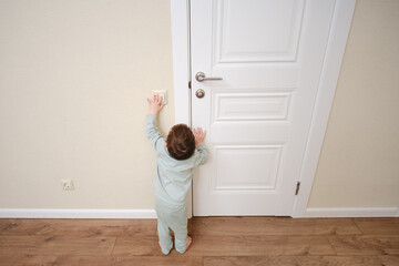 Little baby turns on the light by pressing the switch. Small child turns off the electric light at the white door. Kid aged two years