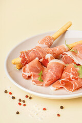 Plate with slices of tasty jamon and Italian Grissini on yellow background, closeup