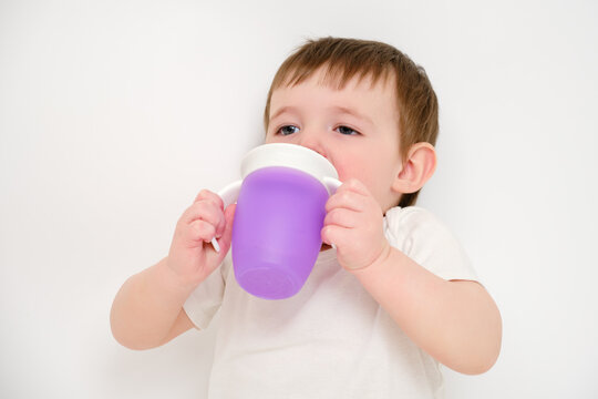 Happy baby drinks water from cup on studio white background. Resting child with cup juice in hands. Kid about two years old (one year nine months)