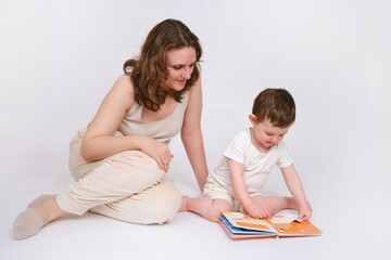 Happy baby with mother reading a book on studio white background. Portrait of a smiling child with mom. Kid about two years old (one year nine months)