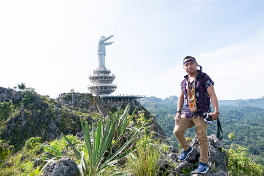 Photo of a young man standing on a hill with a statue of the Lord Jesus in Buntu Burake Toraja in the background