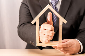 Businessman hand hold for select a home and with thumbs up sign with recommend the good home model on the desk in the office, Loan for real estate or saving money for buy house to family concept.