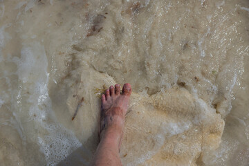 Close up view of feet with sunburn marks of man standing on sandy coast with incoming waves. Aruba. 
