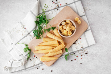 Wooden board with cut and whole canned baby corn cobs on light background