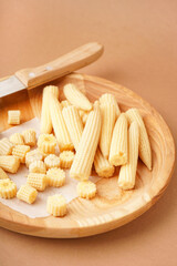 Plate with cut and whole canned baby corn cobs on brown background
