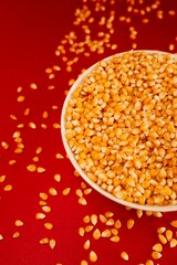 Vertical closeup of a popcorn bowl with some corns spilled around it isolated on a red background