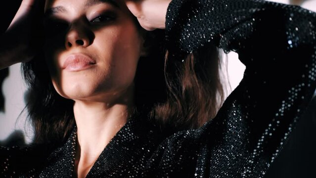 Young beautiful brunette female in trendy evening reflecting dress. Sexy carefree woman posing near white wall in studio in circle a of shadows from tree light. Fashionable model