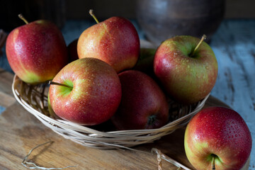 Red apples in a light wicker straw plate on a wooden table