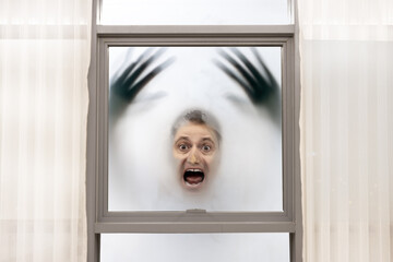 Screaming man with blurred hands has his face pressed against the window on a foggy background
