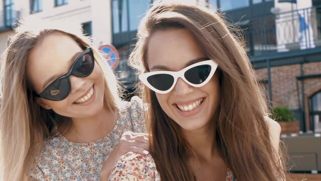 Two young beautiful smiling hipster female in trendy summer sundress. Sexy carefree women posing on the street background in sunglasses. Positive models having fun and going crazy