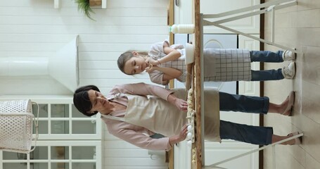 Mature grandmother teaching little preschool grandkid to bake, cooking in home kitchen, preparing pastry food at table with bakery ingredients, enjoying culinary hobby. Vertical full length