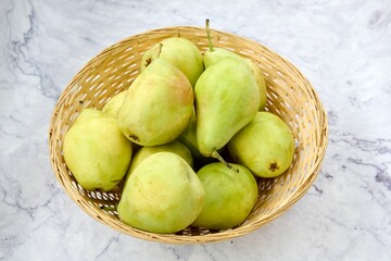 Top view of a wooden basket with green pears on a marble table