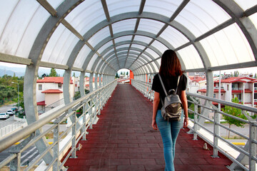 A young woman is walking along a pedestrian bridge in the city.