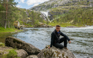 Caucasian hiker posing in front of the beautiful Nykkjesøyfossen waterfall in Husedalen valley, near Kinsarvik. Norway.