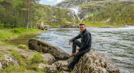 Caucasian hiker posing in front of the beautiful Nykkjesøyfossen waterfall in Husedalen valley, near Kinsarvik. Norway.