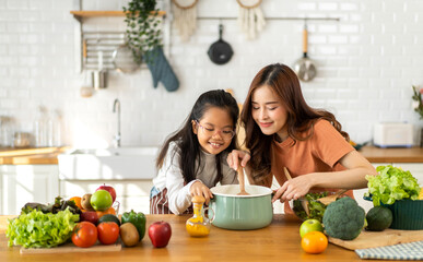Portrait of enjoy happy love asian family mother with little asian girl daughter child help cook food healthy eat with fresh vegetable testing smell soup in a pot with spoon.helping mommy in kitchen