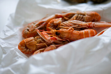 Selective focus of fresh crayfish langoustine in paper wrapping on table in restaurant