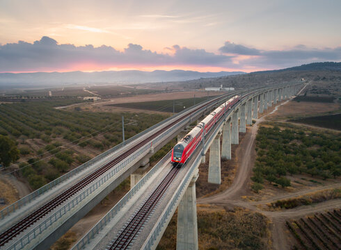 A red train traveling across a bridge in central Israel at sunrise