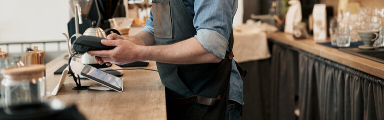 Smiling barista holding payment terminal while standing behind counter