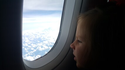 Cute baby looks at sky through the window in plane