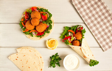 Tortillas, wrapped falafel balls, with fresh vegetables, vegetarian healthy food, on a wooden white background, no people, selective focus.