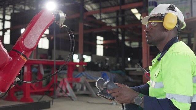 African American factory worker working with adept robotic arm in a workshop . Industry robot programming software for automated manufacturing technology . ..