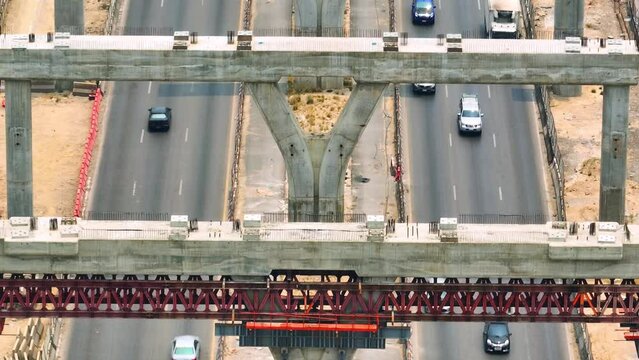 Elevated road construction site is a complex environment with heavy machinery, crane, workers in safety gear, support pillars, and transportation trucks. Drone aerial view. Infrastructure concept
