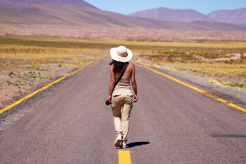 rear view latina woman tourist photographer adventurer walking on the road of the altiplano in Los...
