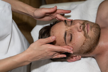 Obraz na płótnie Canvas massage du visage et des tempes d'un homme en salon esthétique