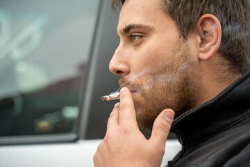 jeune homme fumant une cigarette devant sa voiture © Esta Webster