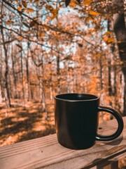 Cup on wooden surface with fall trees in the background