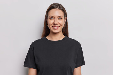 Portrait of good looking young woman with no makeup natural beauty has long dark straight hair dressed in casual black t shirt poses against white background poses in studio for making photo