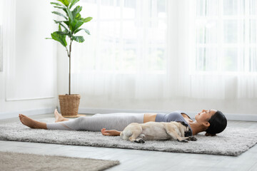 Asian woman doing yoga with her pug breed dog in a peaceful setting, cultivating a sense of harmony and wellness in both body and mind. Self Care Concept.