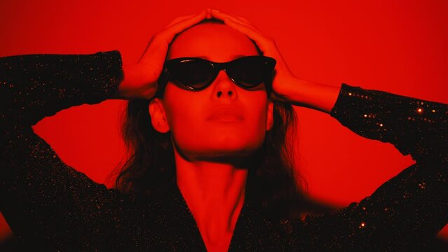 Young beautiful confident brunette female in trendy evening shiny green reflecting dress. Sexy carefree woman isolated on red neon light in studio. Fashionable model. high fashion 