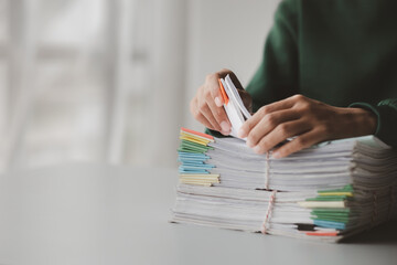 A person sits in an office with a huge stack of papers, she is a company employee, managing paperwork and finance, corporate filing. Document management concept.