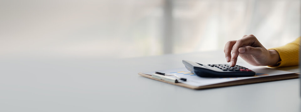Businessman using a calculator to calculate numbers on a company's financial documents, she is analyzing historical financial data to plan how to grow the company. Financial concept.