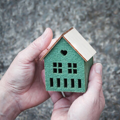 A small house model in female hands on the gray background, selective focus.