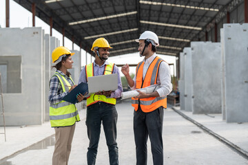 Team of construction engineers wearing vest and helmet safety discussing project at construction site. Group Indian foreman with laptop, paperwork working at factory making precast concrete wall.