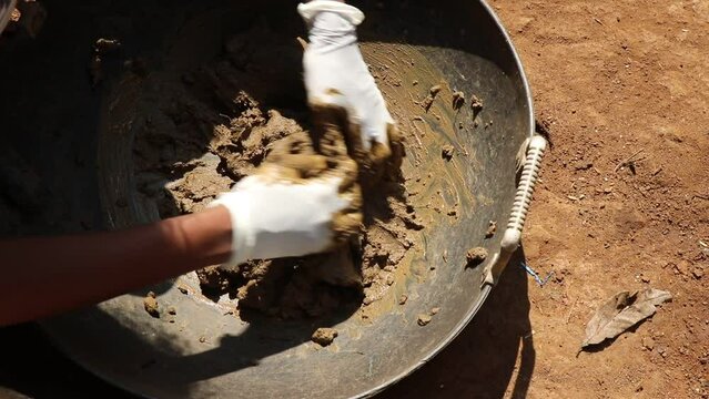 Mixing the clay inside a basket with gloves on hand from natural mud from a paddy farm for making some craft objects