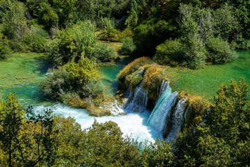 Aerial view of a waterfall flowing through green trees in Krka national park, Croatia on a sunny day