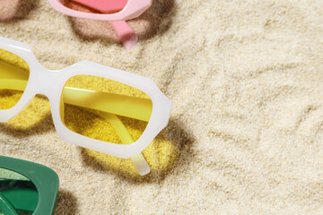 Set of colorful sunglasses on beach sand background at sunlight with shadow. Summer fashion eyeglasses with colored glass. Summer vacation, summer rest concept. Minimal style flat lay