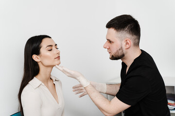 Facebuilding. Doctor examines beauty face of woman. Consultation with plastic surgeon on white background. Cosmetic rejuvenating facial treatment.