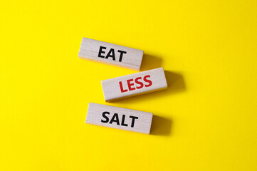 Eat less salt symbol. Concept word Eat less salt on wooden blocks. Beautiful yellow background....