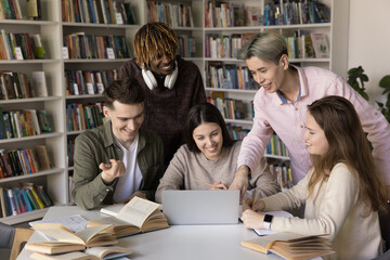 Five happy multiracial students, groupmates look at laptop screen, discuss online task, make presentation, work on joint on-line project met in library for doing collaborative exercise use modern tech