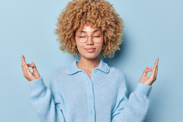 Stress relief concept. Curly haired calm woman meditates with closed eyes practices yoga searches...