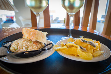 Tapas de ensaladilla rusa y boquerones con patatas fritas con copas de vino blanco