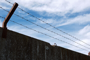 Close-up of a concrete fence with barbed wire against a beautiful sky.